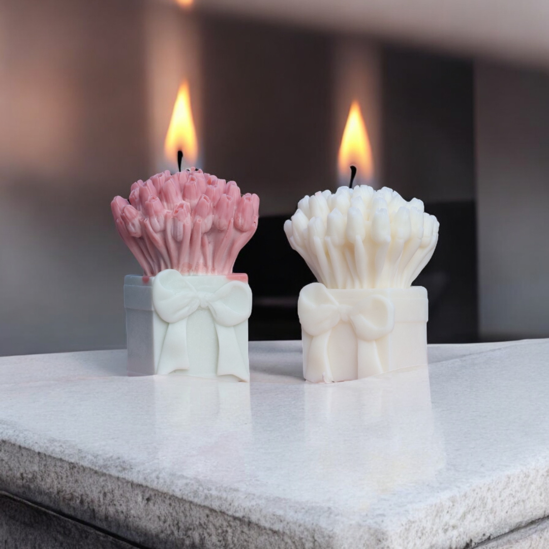 Two shell-shaped candles, one pink and one white, on a reflective surface with a blurred background.